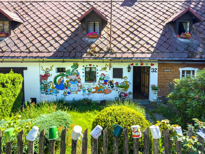 Painted cottage front with flowers in the yard.